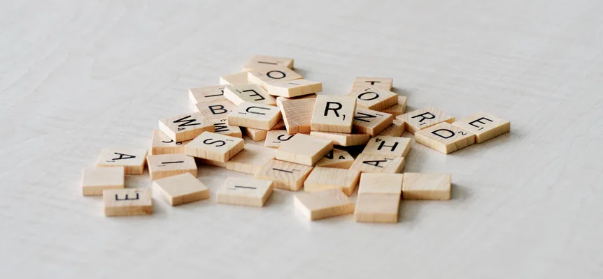 A loose pile of wooden letter tiles with Latin letters on a pale wooden table