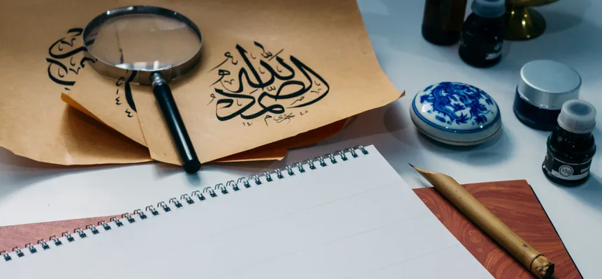 Sheets of Arabic calligraphy laid out with ink bottles and a magnifying glass