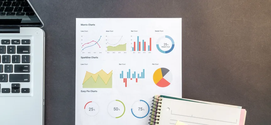 Une feuille imprimée d'exemples de graphiques en courbes, en barres, en secteurs et en anneau sur un bureau sombre, entre un ordinateur portable ouvert et un carnet à spirale