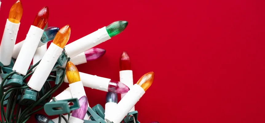 Un enchevêtrement de guirlandes de Noël en forme de bougies, aux ampoules orange, vertes, roses et rouges, sur un fond rouge vif