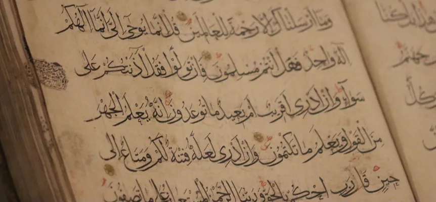 A page of an old handwritten Quran in black script, with red vowel marks and small gold verse markers on yellowed paper