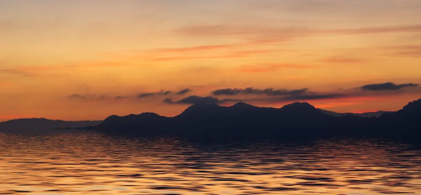 An orange sunset sky over dark mountain silhouettes, reflected in rippling water